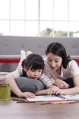 Smiling Asian mother and little asian girl child is drawing and Painting with wooden colored pencils on paper for imagination together in living room. Homeschool and educational concept