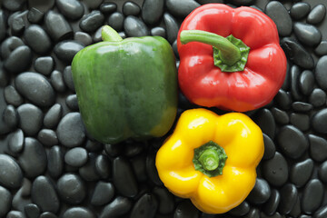 Red, green and yellow bell peppers on black stone. Stone background has smooth glossy skin and round edge.