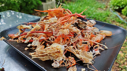 A Pile of grilled shrimp shell waste after eating on black plate.