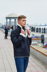 A guy in a warm leather jacket on the embankment with a rotunda holds a collar with both hands....