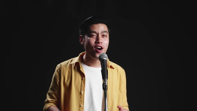 Asian Man Singer Singing Into Microphone On Black Background

