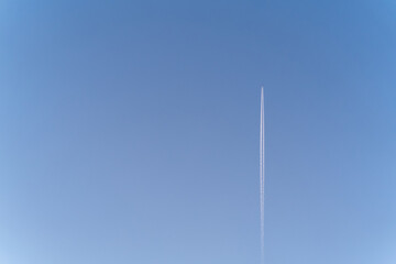 The plane flies far away in the blue sky and leaves a trail