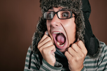 A frightened man in a winter hat shouts with his mouth wide open.