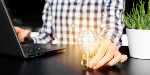 Successful business idea and creative innovation concept, close up business man holding lighting bulb and tablet with financial graph on table
