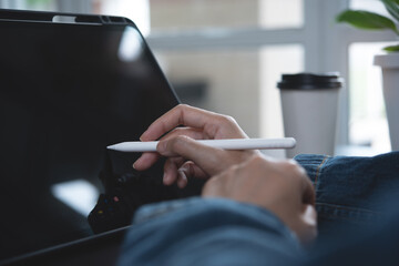 Close up of woman hand with stylus pen touching on digital tablet screen. Female graphic designer designing her work, using tablet pc via mobile app