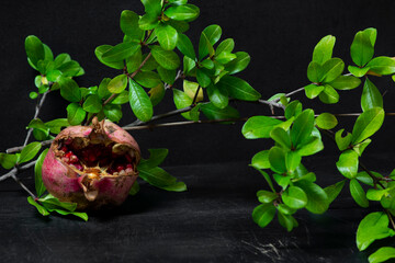 red pomegranate and seeds with green leaves on wooden old cutting board, side view, dark background