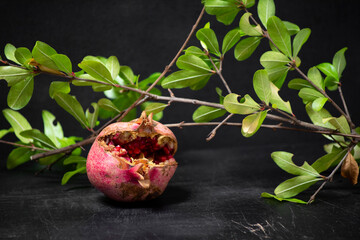 soft focus of red pomegranate and seeds with green leaves on wooden old cutting board, side view, dark background