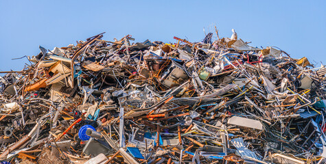Large heap of old iron objects intended for recycling against a bright blue sky. The photo was...