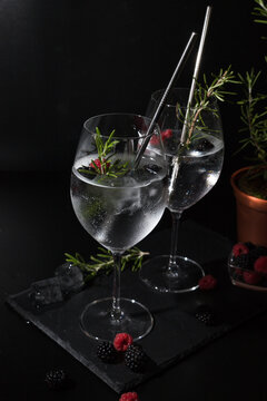 two gin tonc with berry and rosemary on a balck background