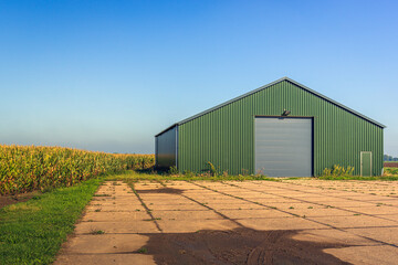 Modern agricultural barn with a yard of concrete slabs. The photo was taken in the Netherlands on a sunny day in the fall season. - obrazy, fototapety, plakaty