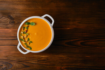 Pumpkin creamy soup in a bowl with seeds and basil