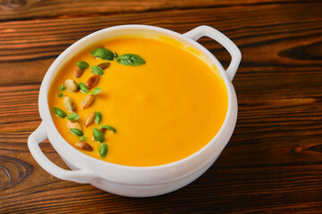 Pumpkin creamy soup in a bowl with seeds and basil