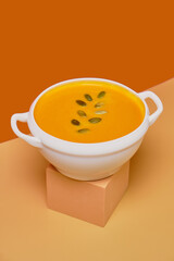 Pumpkin soup decorated basil on orange background