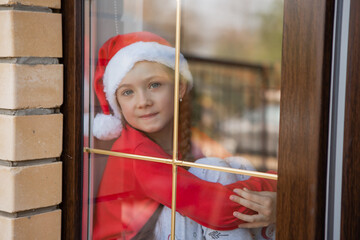girl in red Christmas pajamas looks at the street through a closed window. winter New year's concept. stay home. space for text. New Year in quarantine. High quality photo