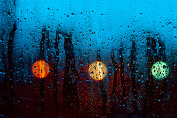 drops of water flowing down the blue glass of the window with the reflection of the light of the lanterns