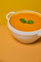 Pumpkin soup decorated basil on orange background