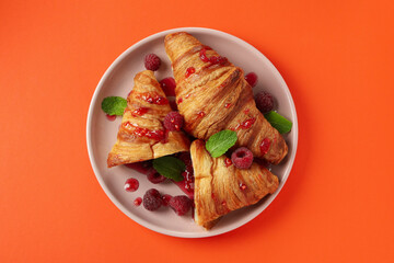 Plate with croissants with raspberry jam on orange background