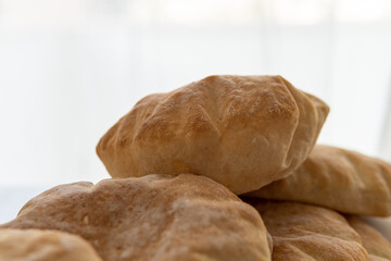 Selective focus on a fluffy pita bread placed on a pile, hot from the oven. Homemade, freshly baked gluten-free flatbread or pitta. Golden, round bread to be stuffed with food with white background.