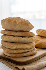 Stack of pita bread on a wooden board, hot from the oven. Homemade, freshly baked gluten-free flatbread or pitta. Fluffy, round bread that can be stuffed with food. Rustic cloth and white background.