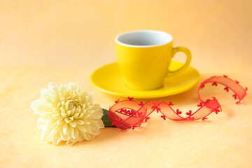 Fototapeta na wymiar 赤いハートのリボンと黄色のダリアの花と黄色のコーヒーカップに入れたコーヒー 