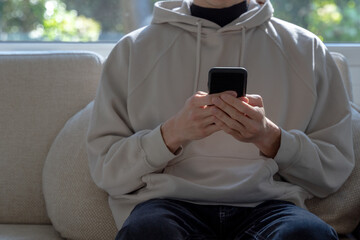 Close up of young hipster man sitting in cozy interior using modern smartphone devices. Social network concept, front view, selective focus