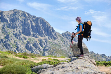 Woman with backpack and poles looking at the mountain in front of her.