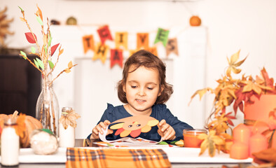 Little cute girl made paper turkey hat for celebrating Thanksgiving day. Diy craft art project.