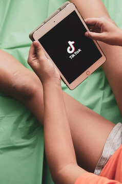 Hands Of A Child Holding An Ipad Tablet With The Tik Tok Logo On The Screen.	
