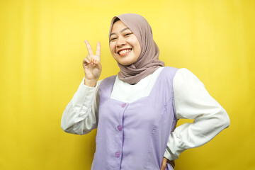 Beautiful young asian muslim woman pouting with v-signed hands, ok, good job, agreement, victory, looking at camera isolated on yellow background