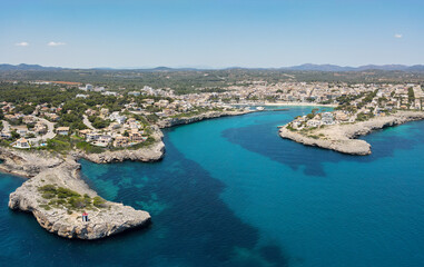 Aerial view of the bay of Porto Cristo on the Spanish Mediterranean island of Mallorca in the sunshine. In the foreground the blue sea and in the background the port and the city.