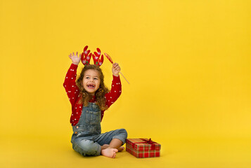 Portrait of happy little  girl Christmas  holding present box and looking at camera on yellow background
