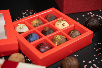 Various handmade chocolate truffle candies in a red box on a dark background. Close up view.