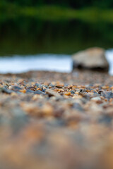 Natural landscape of the lake, high resolution. Reflection of clouds on water ripples. The shore of the lake is made of small stones. In the foreground is a large stone out of focus