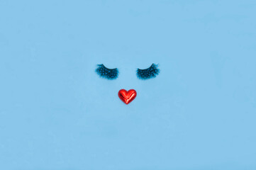 Creative woman face made of eyelashes and red heart lips on the blue background. Minimal beauty concept. Flat lay. Valentine makeup creative concept.