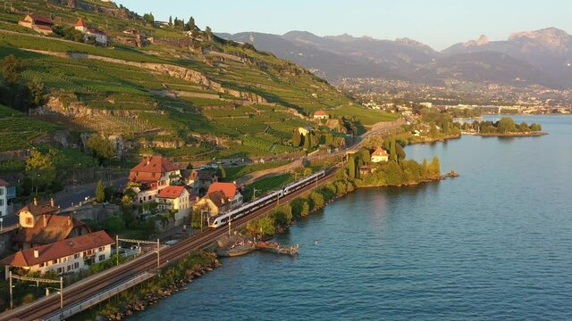 Aerial drone footage of a commuter train riding along the Lavaux famous terrace vineyard by lake Geneva between Montreux and Lausanne in Switzerland. 