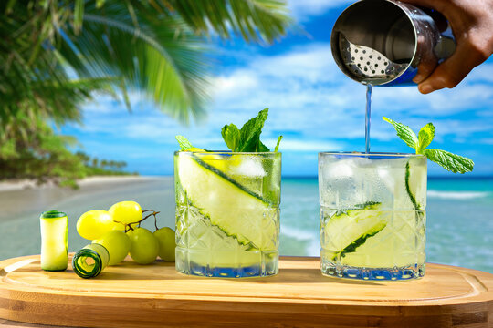 bartender prepares a drink, beach background, two glasses on a wooden board, male hand pours drink into a glass