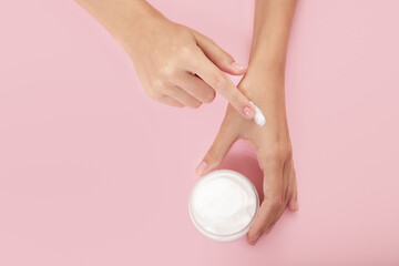 woman hands with perfect manicure open a jar of cream. pink background