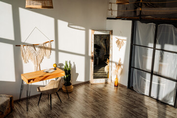 Interior picture of the room in the loft style in the bright rays of the sun. Wooden table, succulents and cacti, a large mirror and a decorative pano on the wall.