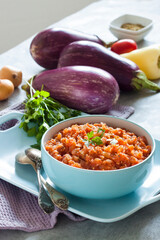 Eggplant caviar in blue bowl and fresh vegetables on background