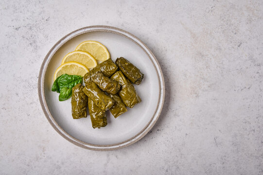 Dolma, stuffed grape leaves with rice, meat, parsley and lemon on light plate. Top view