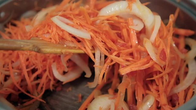 Wooden spoon stirring yam, carrots, tomato, and onion slices in pot