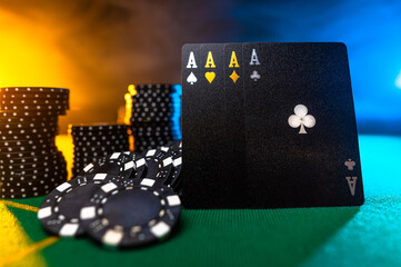 There are black poker cards and chips on the green cloth of the gambling table. Multicolored smoky background. Beautiful composition. Nightclub, casino, poker, risk, luck, gambling business.