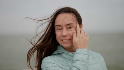Portrait of a beautiful woman with long hair smiling outdoors on a cloudy autumn day. A happy woman on the street.