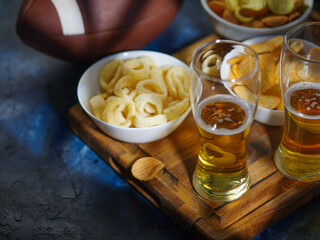 A classic set of sports fans - onion rings, potato chips and beer in glasses. Wooden tray, blue background, baseball glove. Low angle view. Watching sports matches on TV with friends, rest.