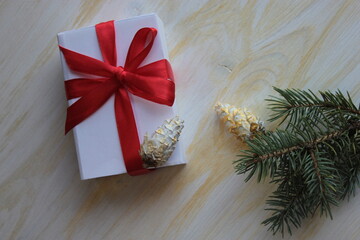 A gift box with a red ribbon, cones and a fir branch.