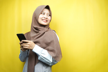 Beautiful young asian muslim woman smiling confident, enthusiastic and cheerful with hand pointing at smartphone, promoting something, hand promoting app, isolated, advertising concept