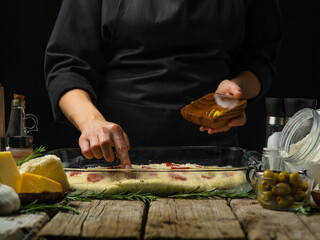 The chef lays out the chopped olives on the dough prepared for baking. ingredients. Wooden texture. Black background. Cooking pizza, pie, focaccia. Close-up.