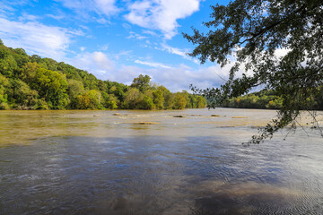 Fototapeta na wymiar a stunning shot of the silky brown waters of the Chattahoochee river with lush green and autumn colored trees along the river with blue sky and clouds at Cochran Shoals Trail in Marietta Georgia USA