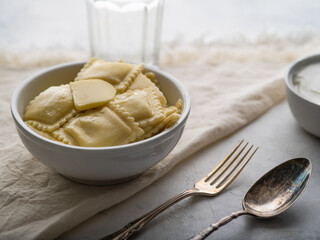 Serving of Italian ravioli in a white plate, fork and spoon. White tablecloth. Daylight illumination. Italian food. Restaurant, hotel, home cooking, culinary blog, recipe book...