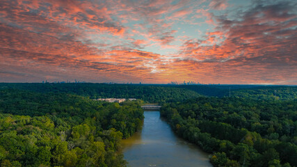 a stunning aerial panoramic shot of the Chattahoochee river surrounded by lush green and autumn colored trees with powerful red clouds at sunset at Cochran Shoals Trail in Marietta USA